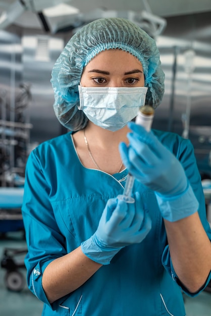 Nurse in mask and gloves holding a syringe with medicine and waiting for a patient in surgery