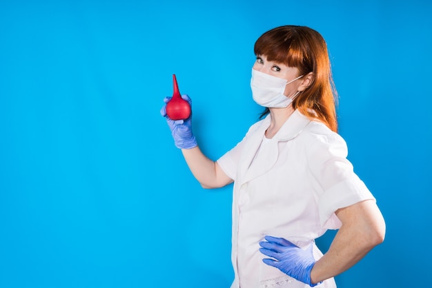 A nurse in a mask holds a medical pear in his hands and looks into the camera