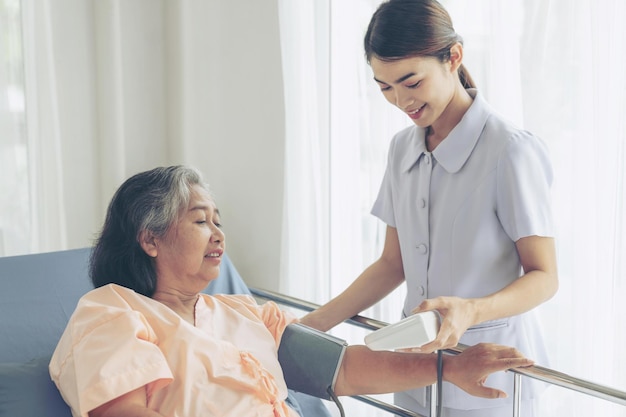 病院のベッドの患者の医療とヘルスケアのシニアコンセプトで年配の女性の血圧を測定する看護師