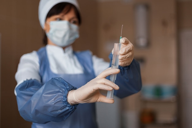 Nurse in medical clothes is about to be vaccinated to find in a hospital ward. Focus on the syringe, the woman's face is blurred.