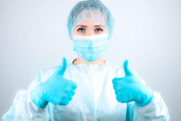 A nurse in a medical gown, mask and protective gloves gives a thumbs up