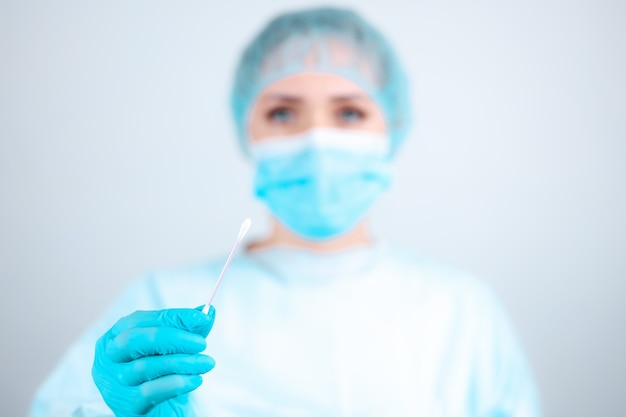 Медсестра в медицинском халате, маске и защитных перчатках держит косметический ватный тампон.