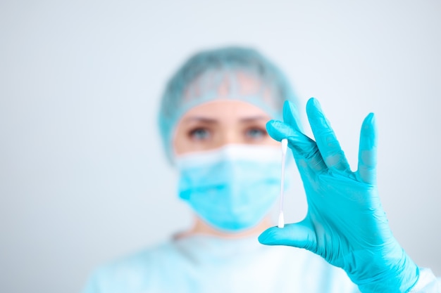 A nurse in a medical gown, mask and protective gloves holds a cosmetic cotton swab