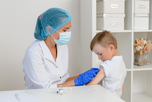 Фото Медсестра или врач наклеивает пластырь на руку ребенка после введения вакцины от коронавируса