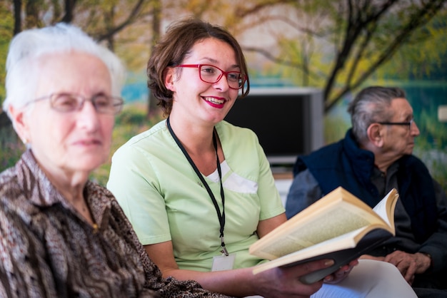 Photo nurse reading book to elderly group of people