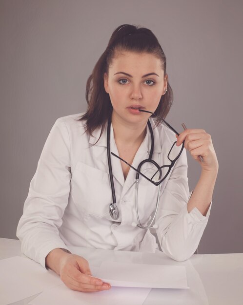 Nurse in robe and glasses and stethoscope is checking her report and thinking about it at the table