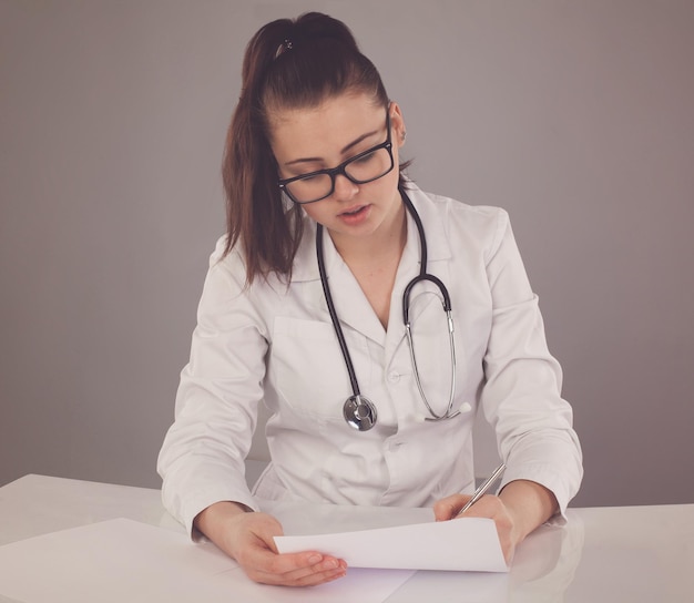 Nurse in robe and glasses and stethoscope is checking her report and thinking about it