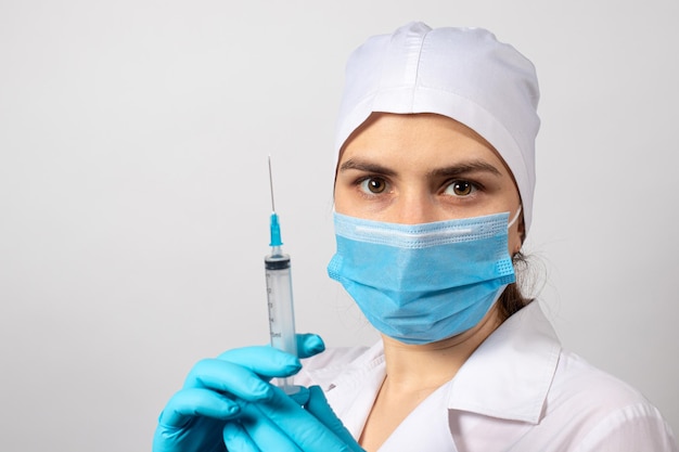 A nurse in a robe and a medical cap and gloves holds a syringe