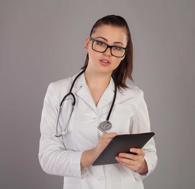 Nurse in robe and with stethoscope is writting something against of grey background