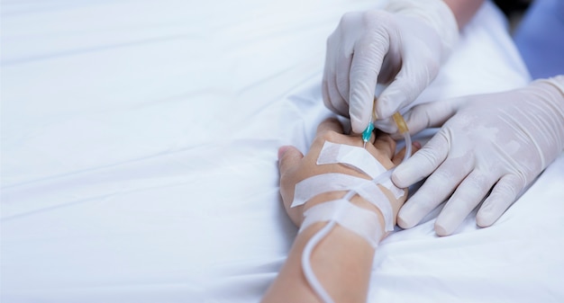 A nurse's hand gently pricks a medical needle into a sick patient's hand to prepare a saline solution and medicine for the debilitated patient