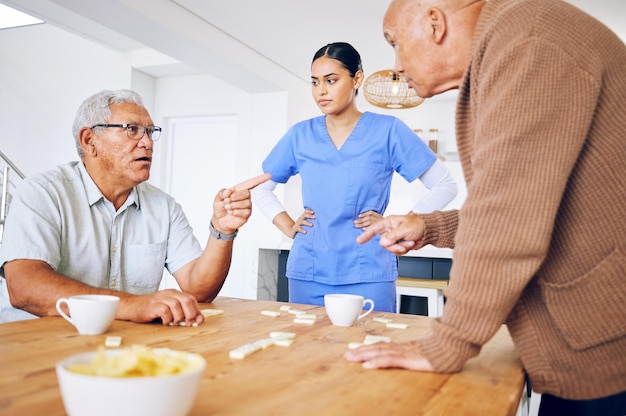 Nurse senior and fighting over a game of dominoes with people in a retirement home for assisted living Healthcare medical and a female medicine professional looking at upset old men arguing