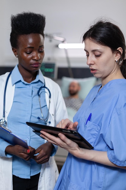 Photo nurse showing lab results from digital tablet to doctor holding clipboard with medical history in modern hospital ward. health care specialists using modern technology for clinical diagnosis.