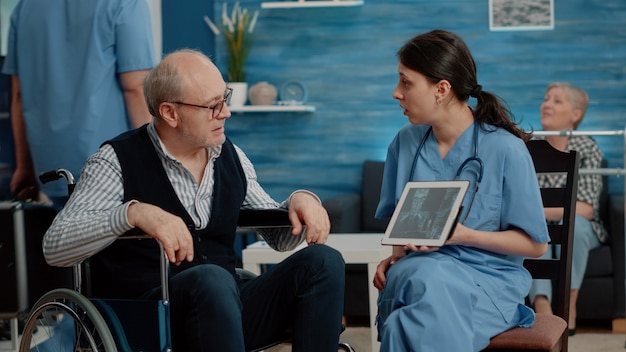 Nurse showing osteopathy x ray on tablet to disabled old man