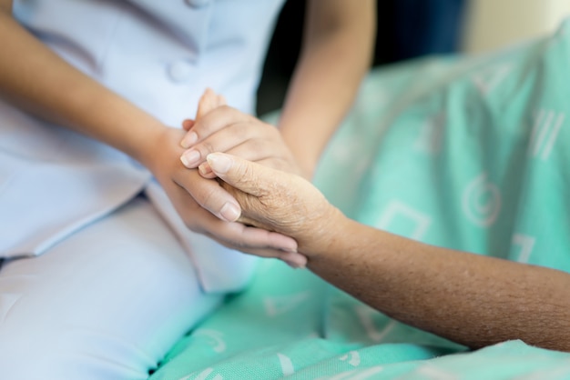 Nurse sitting on a hospital bed next to an older woman helping hands