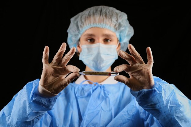 A nurse virologist in a mask holds a thermometer stop coronavirus temperature screening