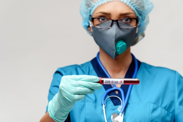 Nurse wearing protective mask and gloves and holding positive coronavirus COVID-19 blood test