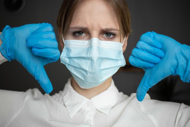 Медсестра в защитной маске и перчатках указывает двумя пальцами вниз