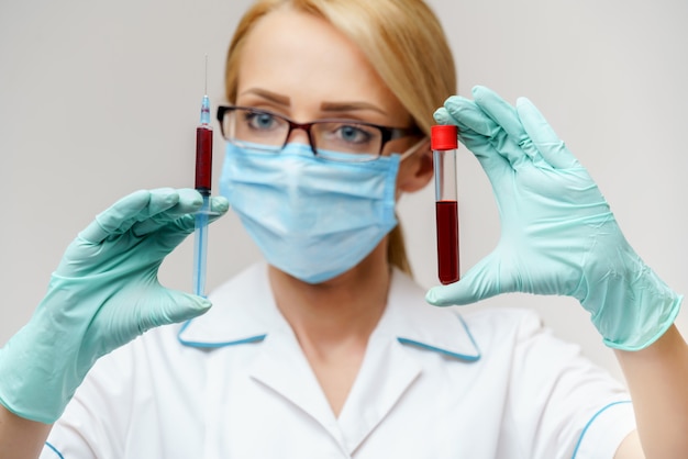 주사기와 혈액 검사 튜브를 들고 보호 마스크를 착용하는 간호사