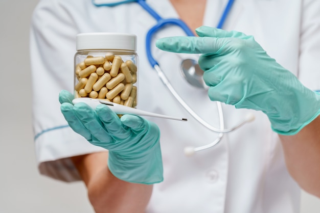 Nurse wearing protective mask and latex gloves and holding can of medicine and thermometer