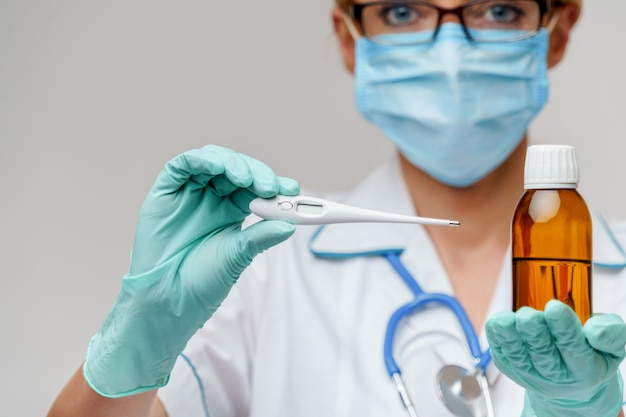 Nurse wearing protective mask and latex gloves and holding can of medicine and thermometer