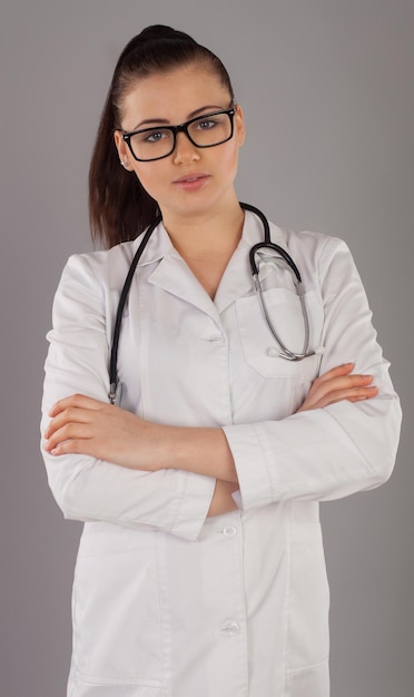 Nurse in white robe with glasses wears stethoscope against of grey background