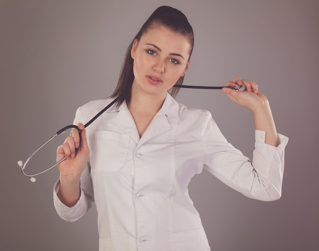 Nurse with stethoscope on her neck is against of grey background