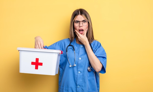 Donna dell'infermiera con la bocca e gli occhi spalancati e la mano sul mento. concetto di kit di pronto soccorso