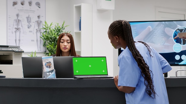 Nurse working at reception counter desk with greenscreen on
laptop, using computer with chroma key display. medical staff in
waiting room lobby with isolated mockup template and
copyspace.