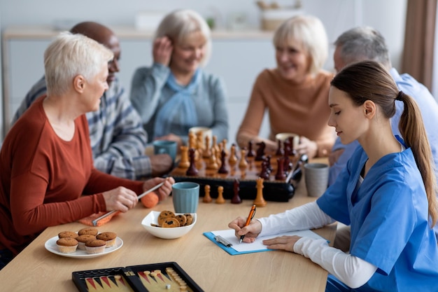 Nursing home worker filling papers while senior people playing chess