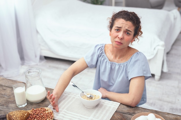 Allergia alle noci. giovane donna che sembra infelice a un tavolo per la colazione mentre si rifiuta di mangiare noci e noci contenenti pane con la sua farina d'avena