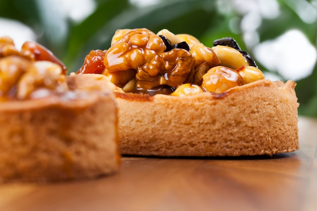 Nut tartlet covered with a layer of liquid caramel, high-calorie dessert made of dough with natural ingredients, tartlet stuffed with hazelnuts, peanuts and walnuts and dried fruits