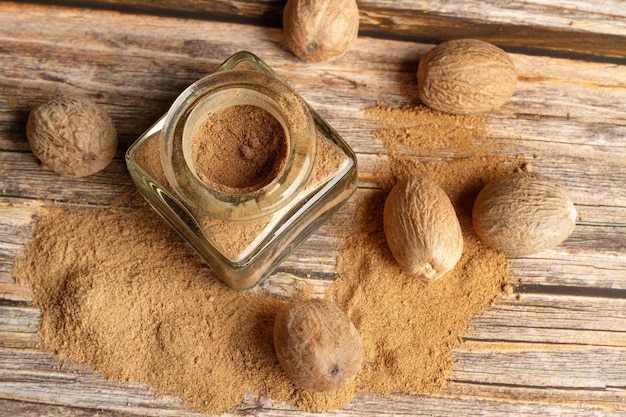 Nutmegs and powdered nutmeg in a crystal bottle on a wooden table in a top view