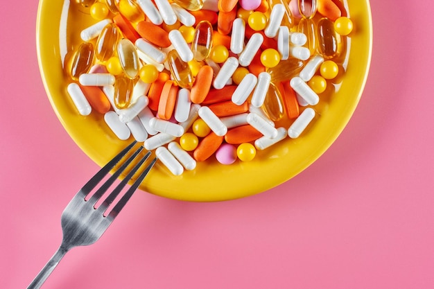 Nutriciologisch concept. Vitaminen voedingssupplementen als capsules op een gele schaal met een vork op een roze achtergrond