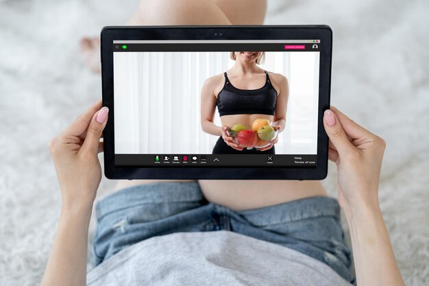 Приложение по питанию Фитнес-телеконференция Здоровое питание Неузнаваемая женщина смотрит на спортивного инструктора с вазой с фруктами на экране планшета