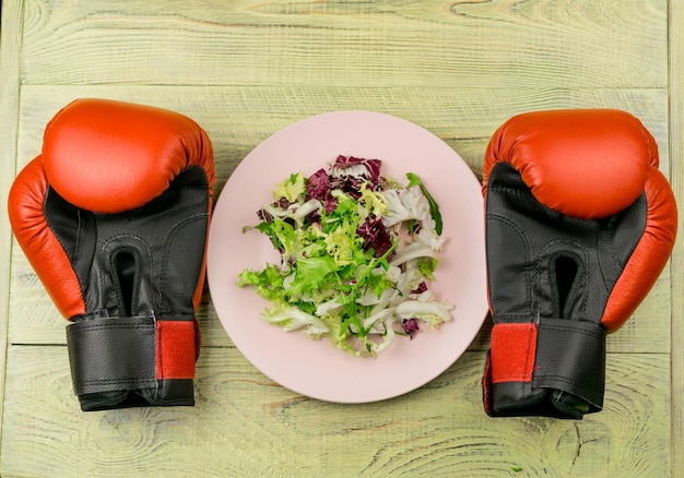 Nutrition for sports healthy active way of life vegetarian\
salad of fresh vegetables and boxing gloves on a wooden\
background