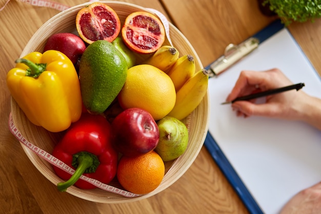 Foto nutrizionista, dietista che scrive un programma di dieta, con verdure e frutta sane, concetto di assistenza sanitaria e dieta. nutrizionista femminile con frutta che lavora alla sua scrivania, posto di lavoro