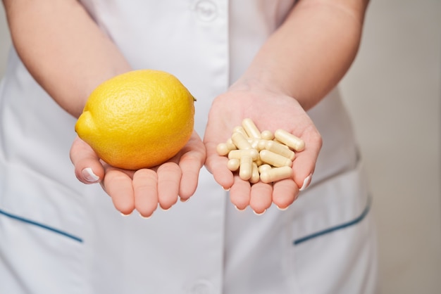 nutritionist doctor healthy lifestyle concept - holding fresh organic lemon fruit and vitamin capsules