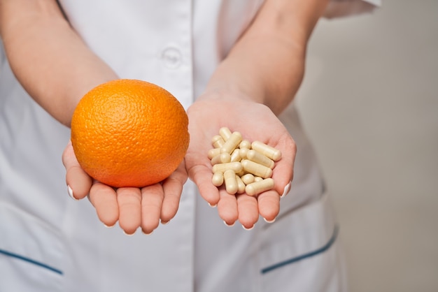 nutritionist doctor healthy lifestyle concept - holding fresh organic orange fruit and vitamin capsules