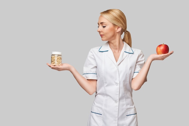 nutritionist doctor healthy lifestyle concept - holding organic red apple and vitamin or medicine capsules pills