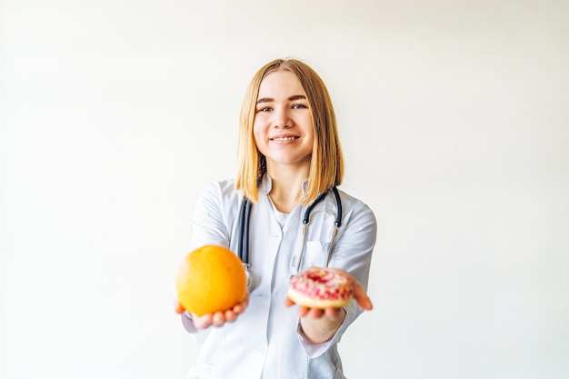 Nutritionist female doctor holding orange and donut in hands, diet concept.