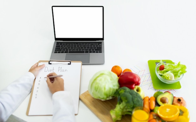 Nutritionist working on laptop and writing diet plan for patient