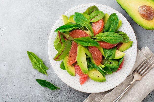 Nuttige smakelijke salade van spinazie, snijbiet, avocado en grapefruit met olijfolie op oude betonnen grijze ondergrond. Selectieve aandacht. Bovenaanzicht.