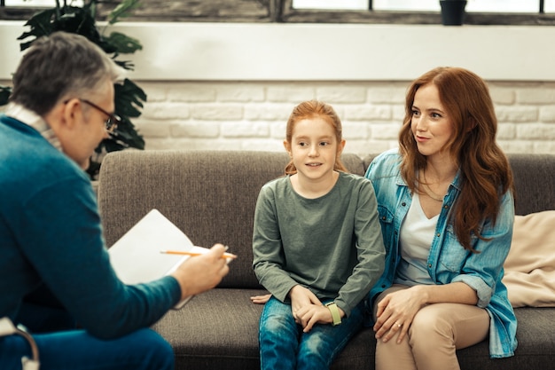 Nuttige therapie. Leuke vrolijke vrouw die samen met haar dochter zit terwijl ze naar de psycholoog kijkt