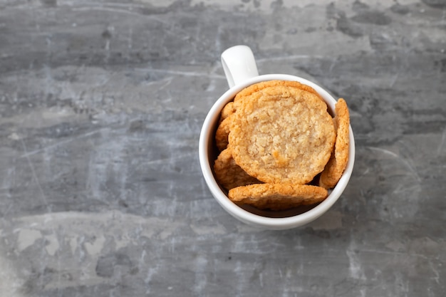 Oat cookies in the white cup on ceramic background