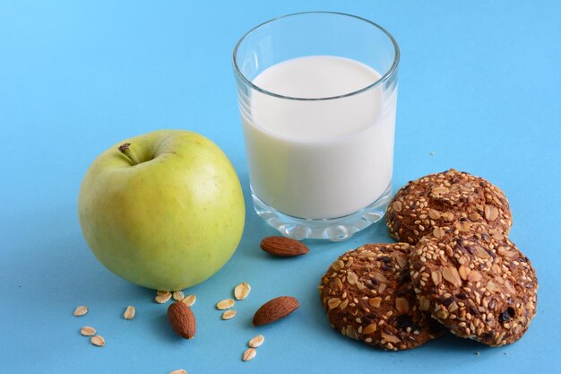 oat cookies with glass of milk and apple on blue background, close-up