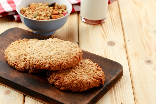 Oat cookies with oat flakes and cup of milk on wooden table close up