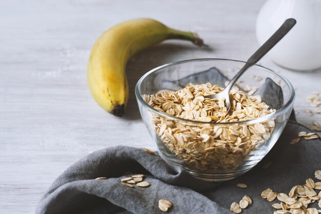 Oat flakes in a glass bowl and banana on the wooden table