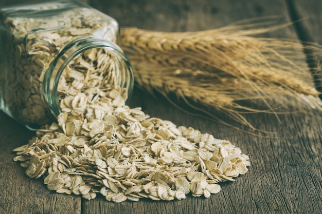 Oat flakes or oatmeal or rolled oat in glass bottle pour on  wood table. 