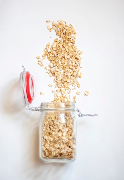 Oat flakes spilled out of the jar, isolated on a white background, flat lay