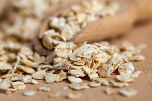 Oat flakes in a wooden bowl with a scoop on the wooden board.